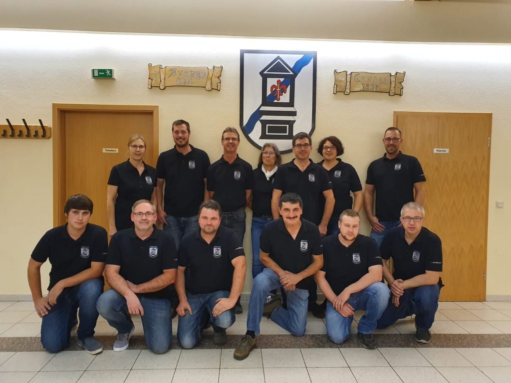 Gruppenfoto der Dorfgemeinschaft Arenza e.V. vor dem Ernzer Wappen im Dorfgemeinschaftshaus